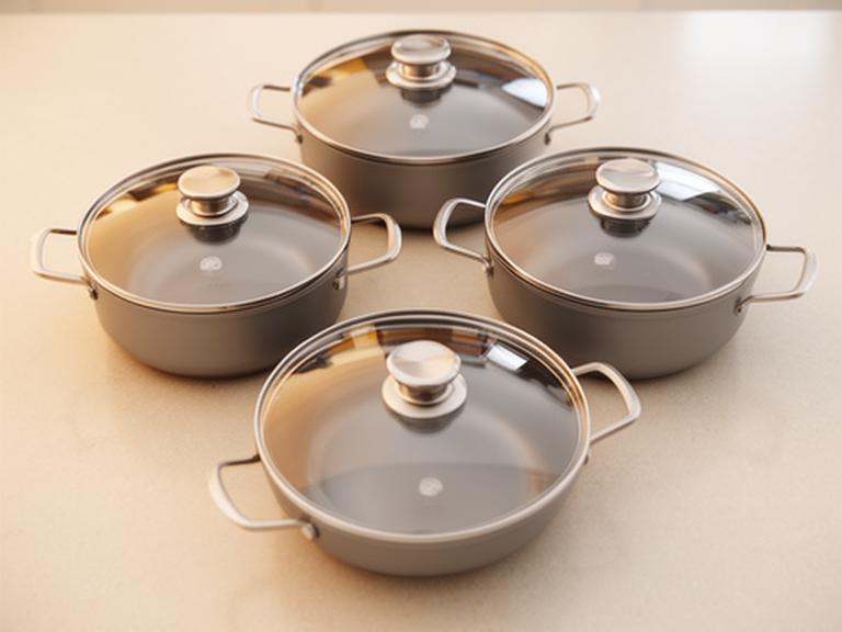 Batería de cocina de 5 piezas ordenada en una encimera clara con tapas alineadas y brillo suave