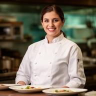 Cocinera de restaurante sonriendo junto a una estación de emplatado en una cocina profesional